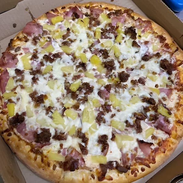 A Bella Pizza Hawaiian pizza with ham, pineapple, and ground beef in a cardboard box.