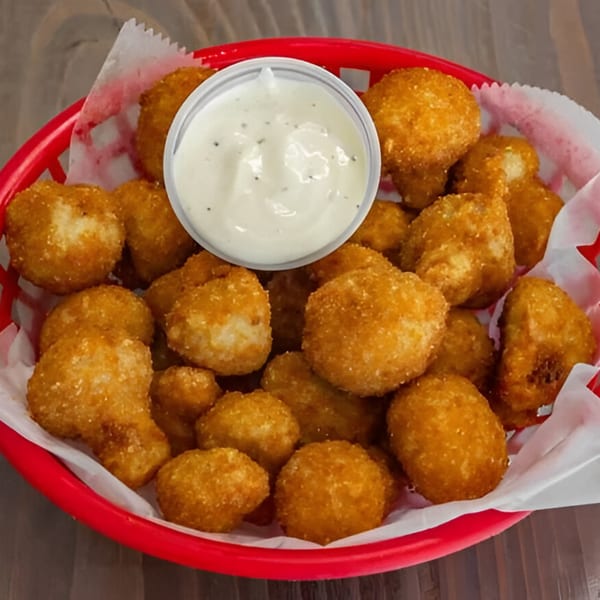 A red basket filled with golden-brown fried mushrooms and a small cup of white dipping sauce.