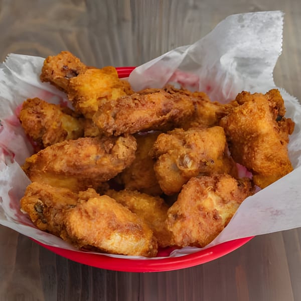 Golden-brown fried chicken wings in a red basket lined with white paper, on a wooden table.