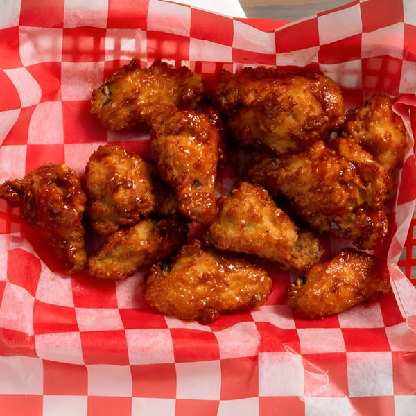 A basket of Bella Pizza's crispy, glazed chicken wings in a red and white checkered paper liner.